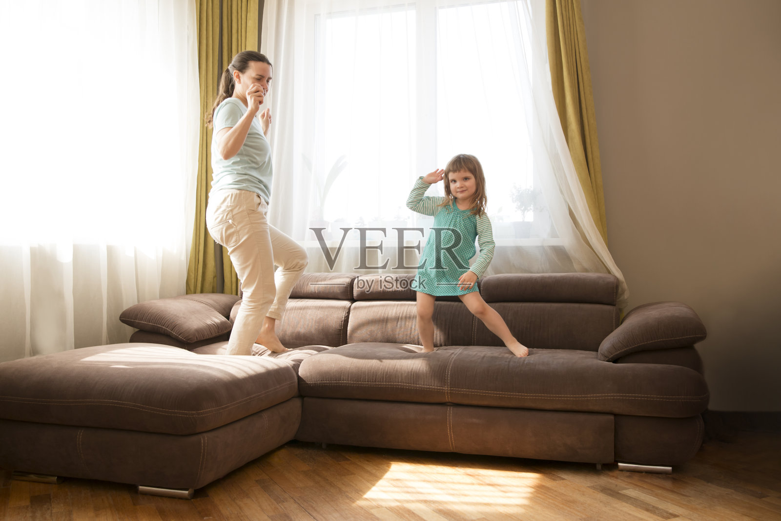 快乐的妈妈和可爱的小女儿一起在房间的沙发上跳舞。隔离。家人在家里玩得很开心照片摄影图片