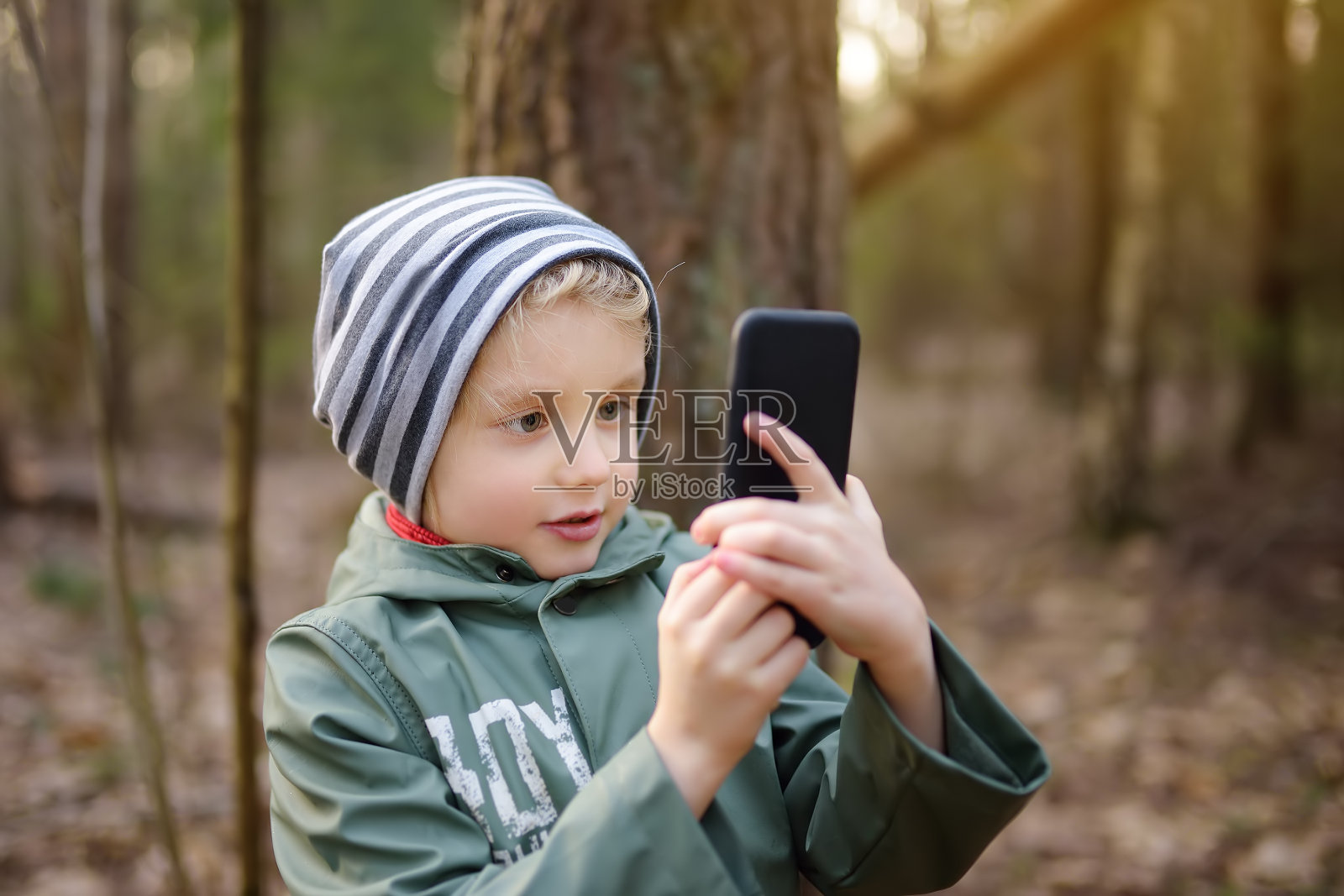 春天或秋天，小男孩在森林里用智能手机拍照或视频通话。照片摄影图片