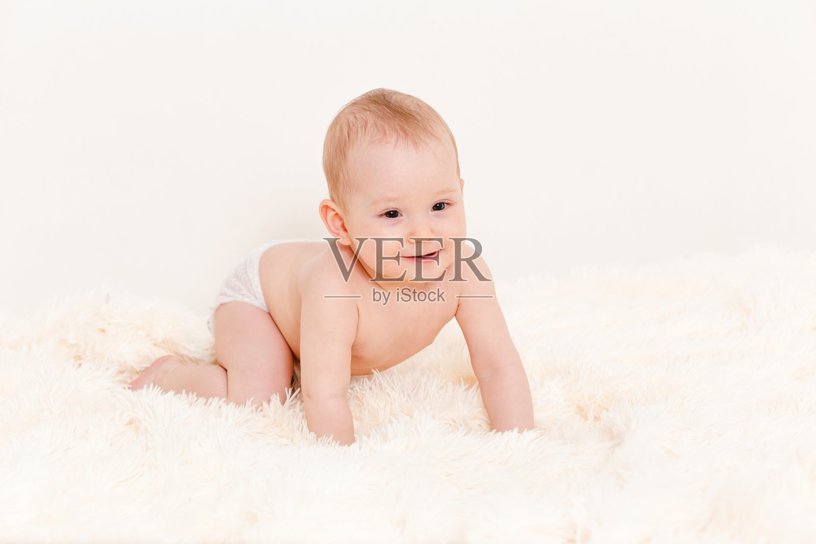Europoid可爱的婴儿在家里的毛茸茸的毯子上爬行。宝宝在一块尿布里。照片摄影图片
