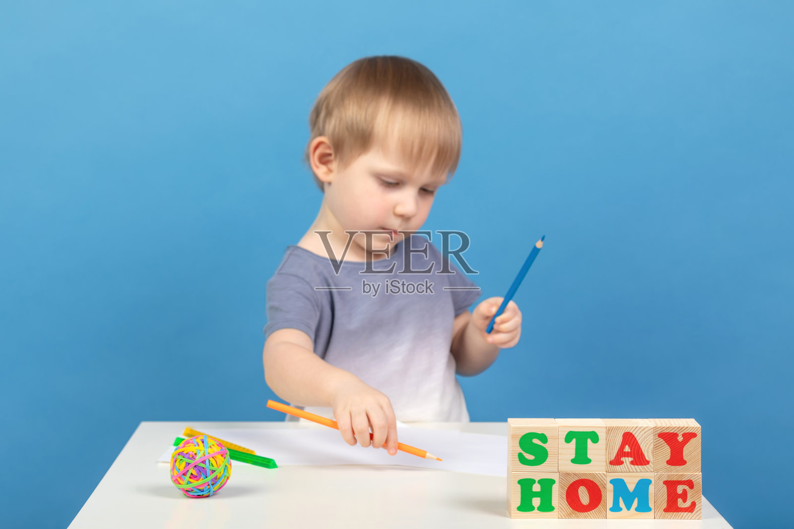 漂亮的金发男孩用彩色铅笔在一张白纸上作画，画面模糊。因为冠状病毒隔离呆在家里的概念。照片摄影图片