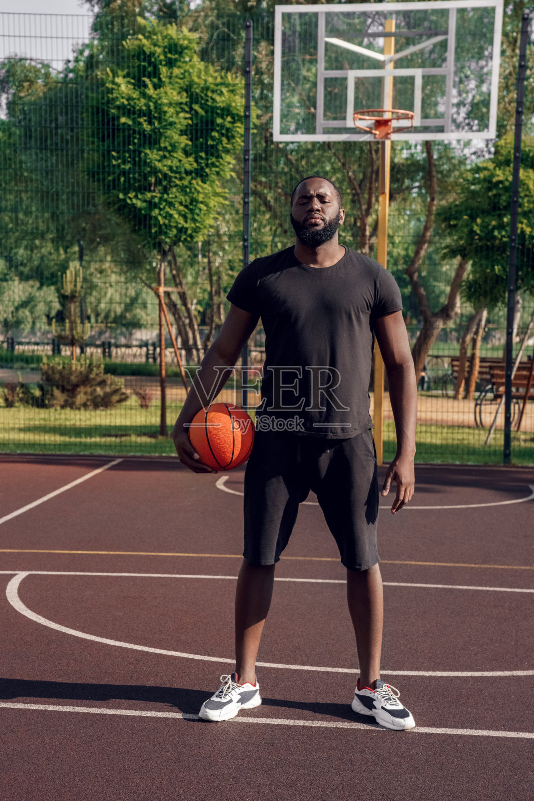 户外活动。非洲人站在篮球场上与球摆出自信的姿势照片摄影图片
