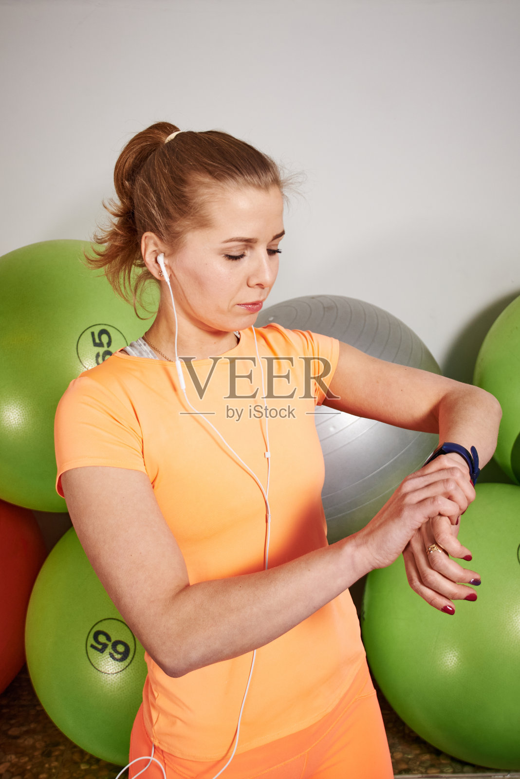 苗条的运动员年轻女子在运动服装与空气pods看起来在健身俱乐部的智能手表。照片摄影图片