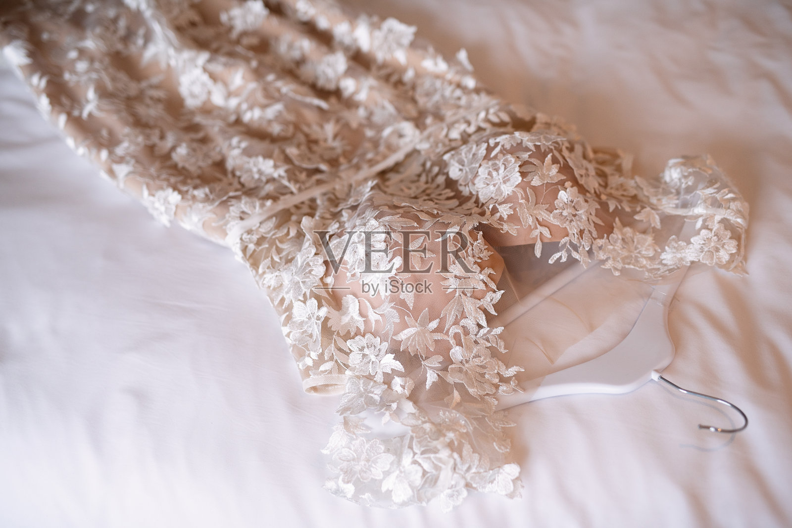 新娘的行头，婚纱躺在床上，白色的被褥，在新娘的房间里，婚礼前的早上，婚纱上装饰着织物花，照片摄影图片