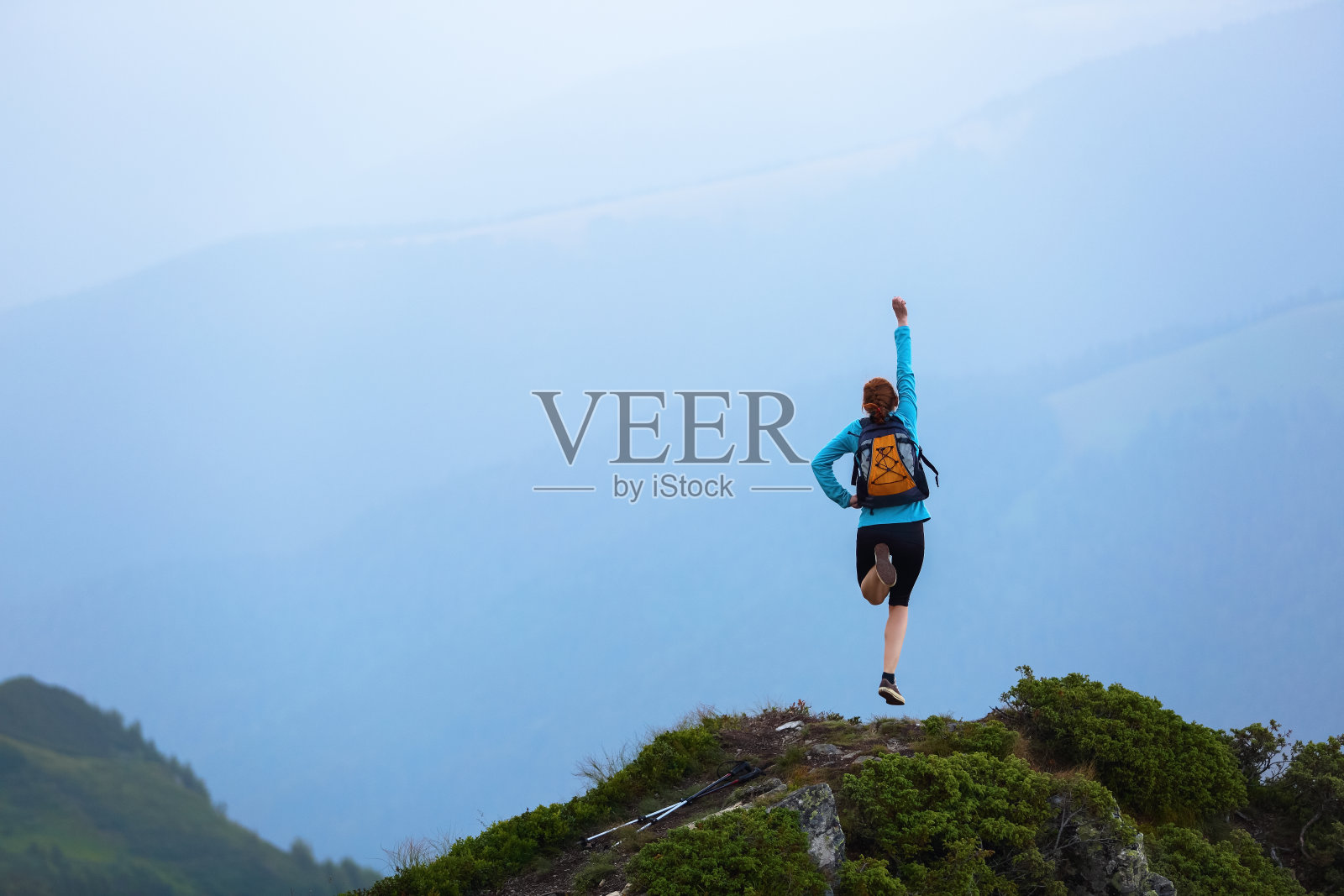 红发女背袋单腿跳，像超人在悬崖边的高山间跳跃。照片摄影图片