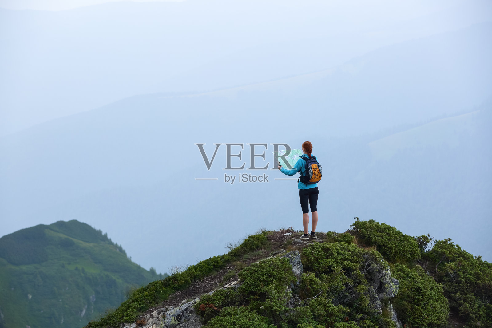 在山顶上，带着地图和指南针的旅游女孩正在寻找梦想的道路。雾中的地平线。夏天的风景。极限运动。照片摄影图片