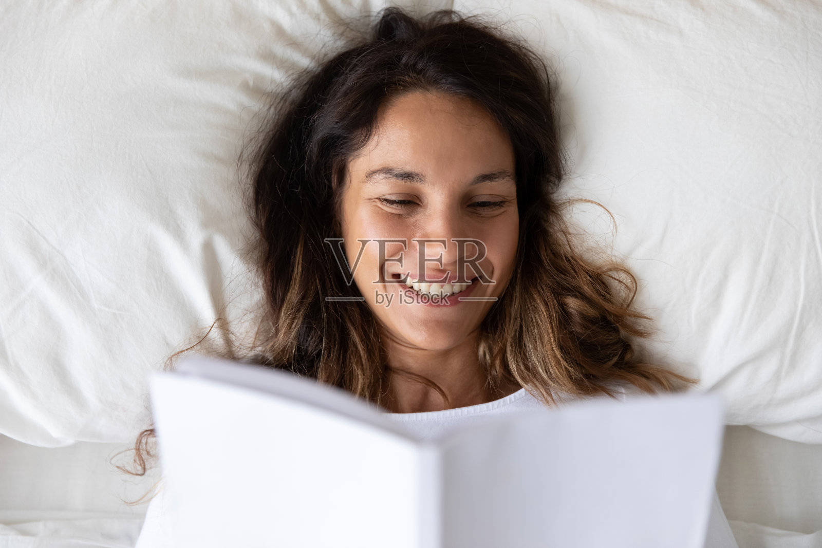 俯视图微笑的女人看书，在床上休息照片摄影图片