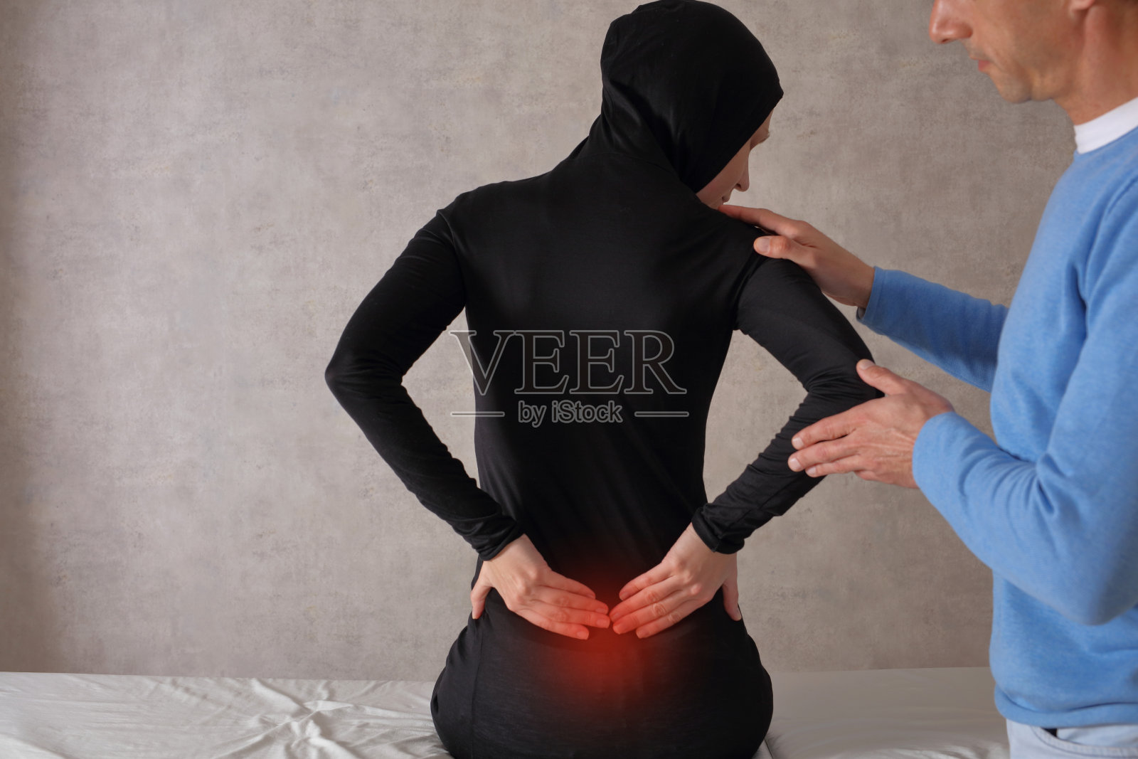穆斯林妇女在医疗检查中背部疼痛。脊椎按摩，物理治疗，损伤康复。照片摄影图片