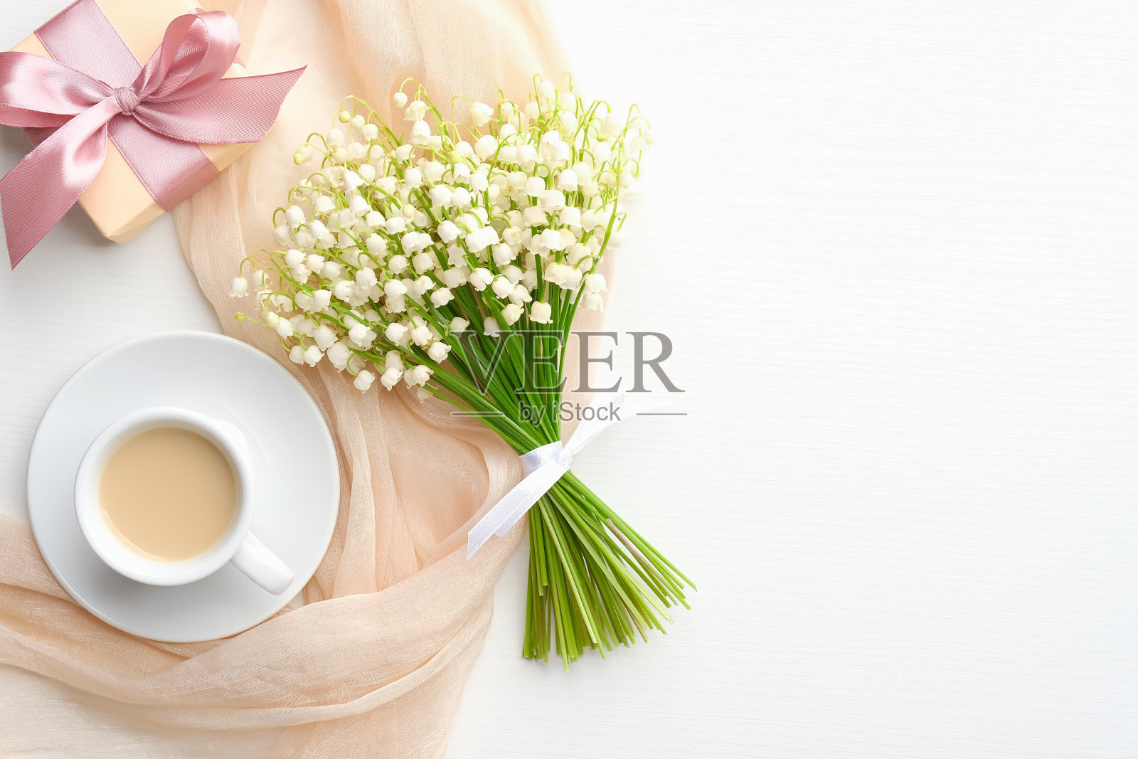 平铺构图，咖啡杯，米色布，山谷百合和礼盒放在白色的桌子上。母亲节庆祝理念。照片摄影图片