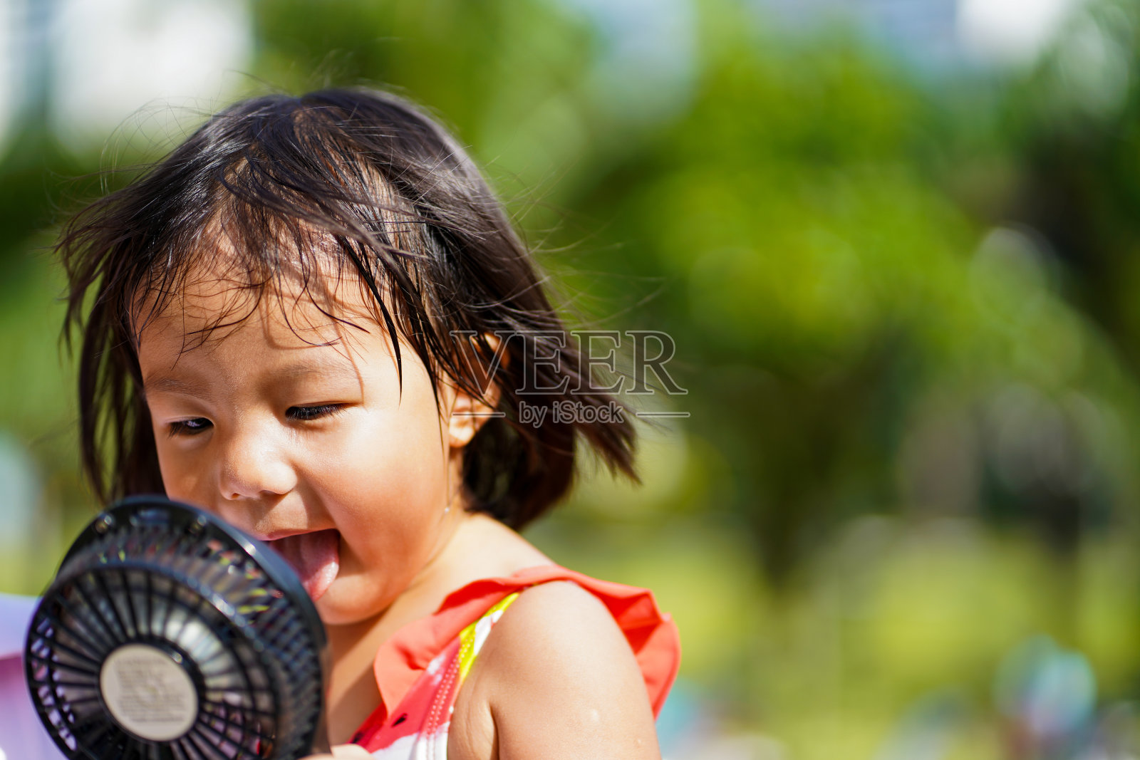 年轻的亚洲女孩试图用便携式风扇扇自己在炎热的天气。照片摄影图片