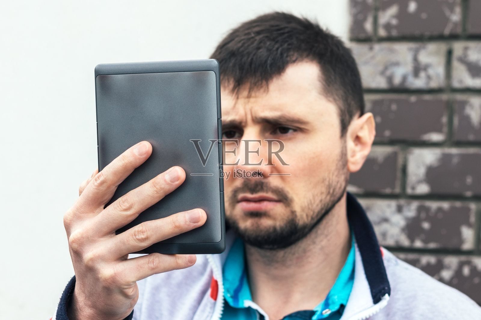 一个严肃专注的人一手拿着一本灰色的电子书放在面前。用口袋阅读器或平板电脑到处阅读书籍或新闻。有选择地用平板电脑集中在手上照片摄影图片