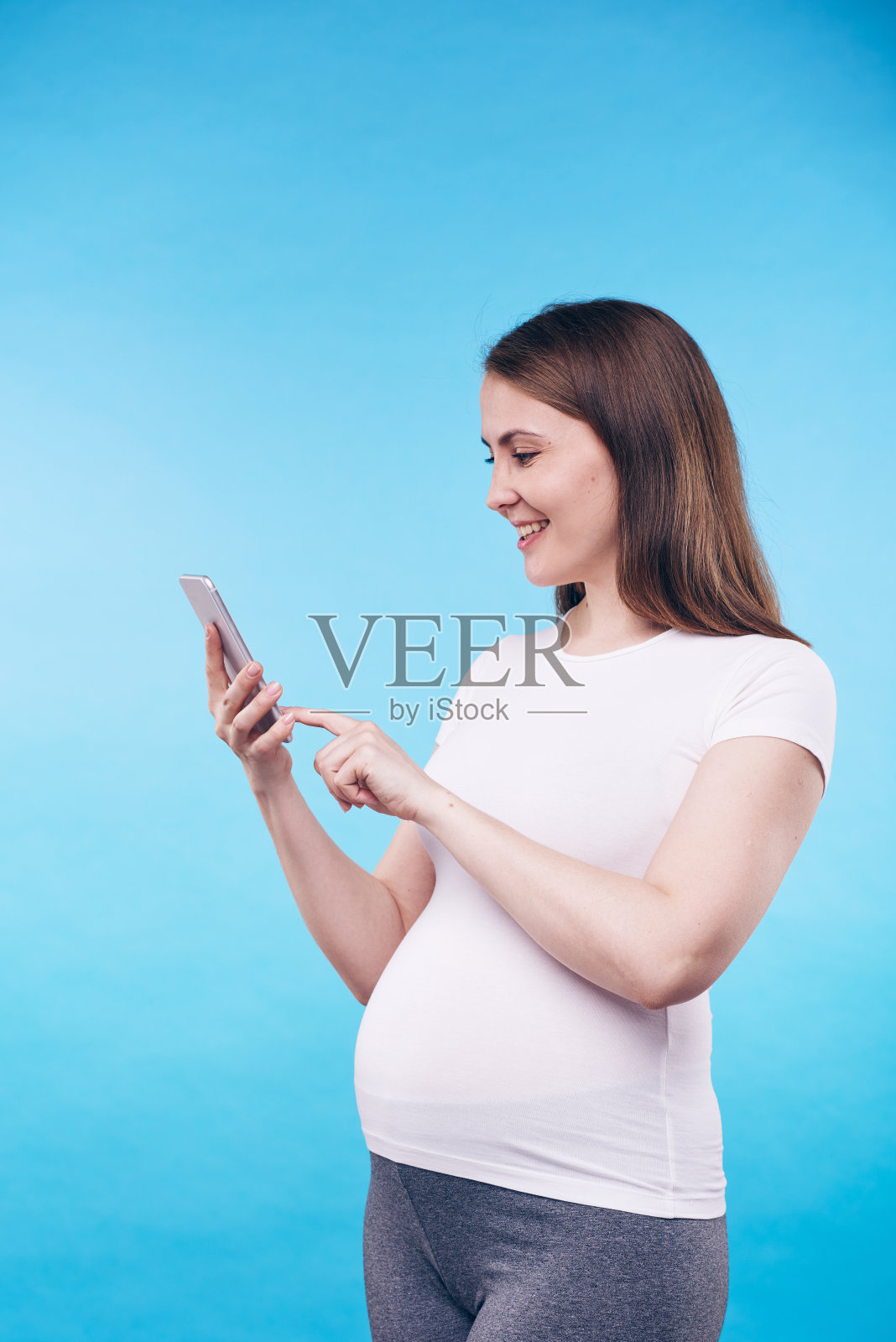快乐的年轻孕妇按智能手机屏幕上的按钮照片摄影图片