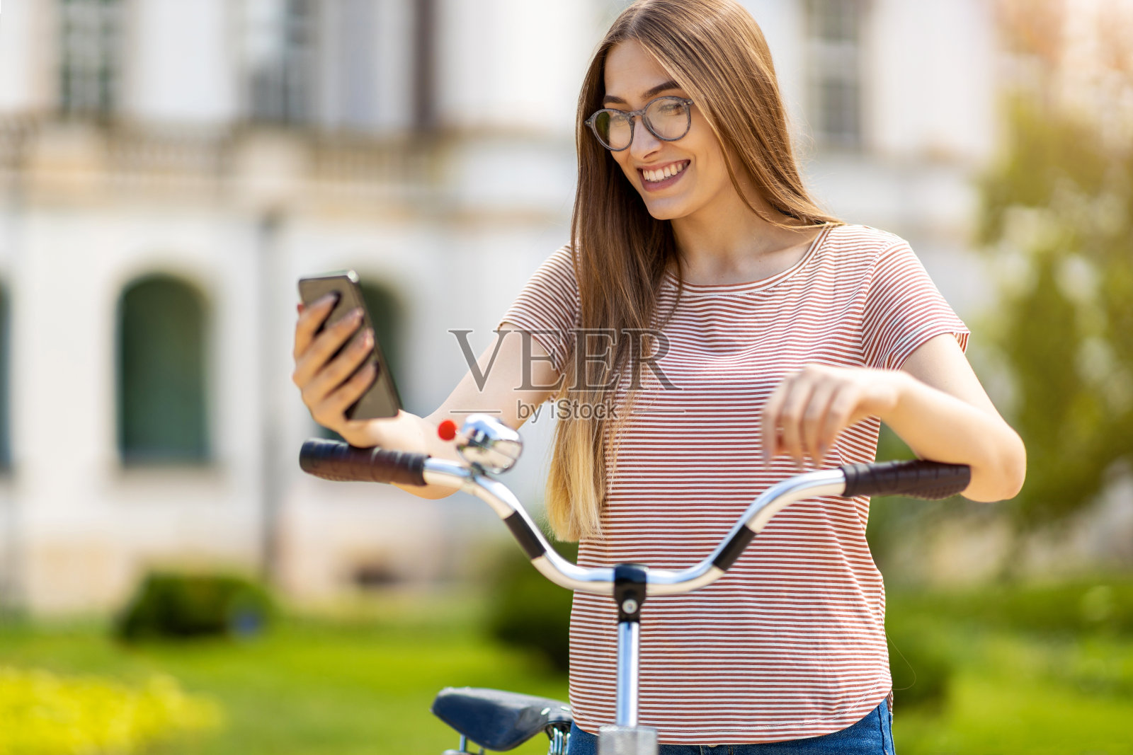 迷人的年轻女子使用智能手机在城市中骑行照片摄影图片