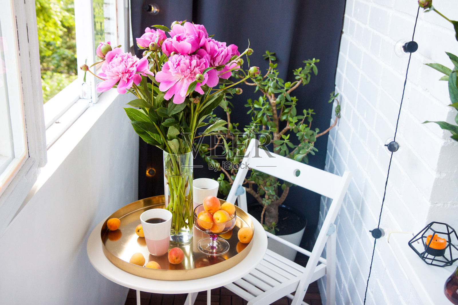 阳台上的夏日早餐。两杯饮料，一束粉红色的牡丹，旧书和新鲜的水果在白色的桌子上。照片摄影图片