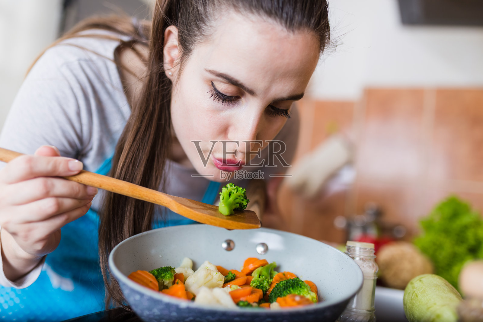 女人品尝食物，同时准备自制的素食餐。照片摄影图片