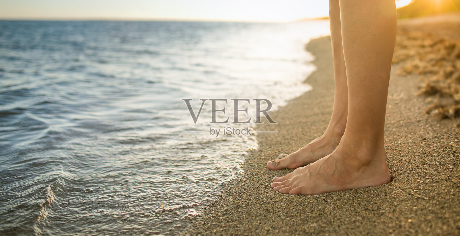女人的脚站在海滩上的特写在日落。照片摄影图片