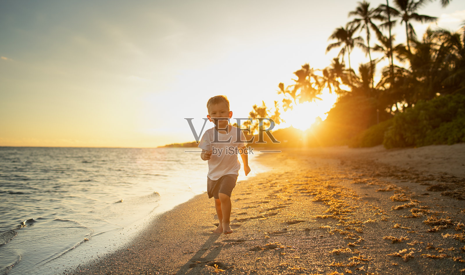 日落时分，小男孩在沙滩上奔跑玩耍。照片摄影图片