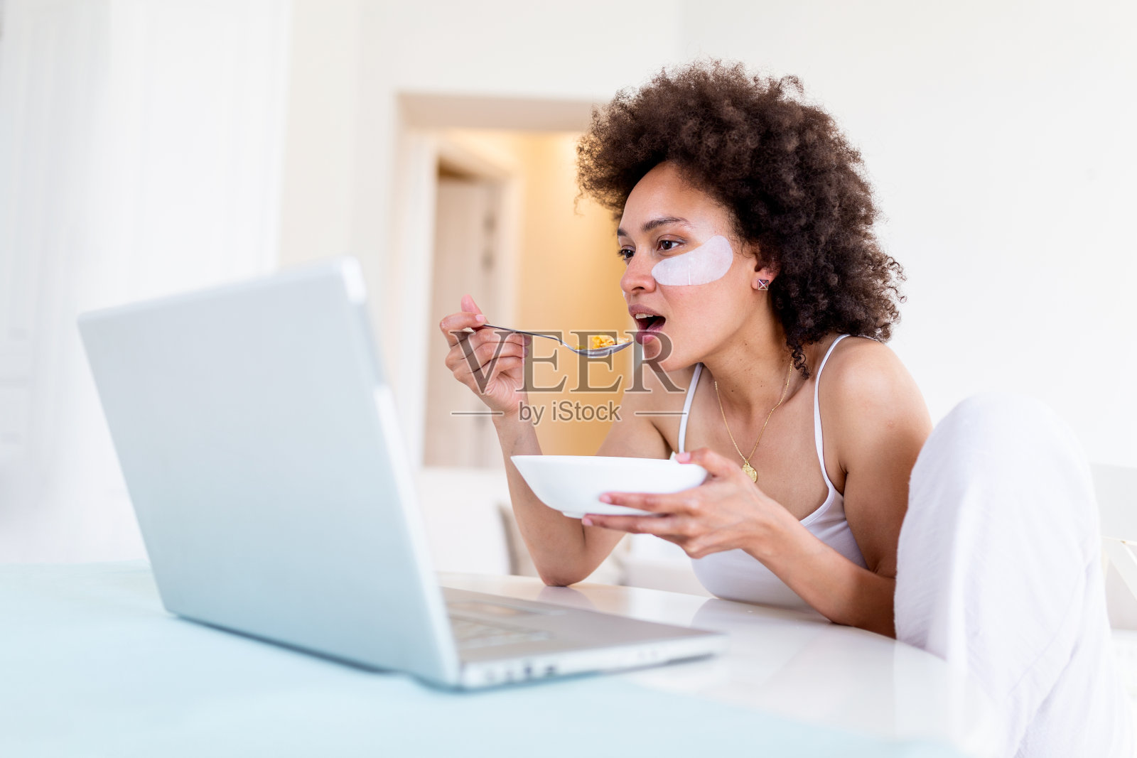 有魅力的女人使用她的笔记本电脑，在家里吃早餐和学习。自由女模特女孩在她的笔记本电脑在早上工作。一杯牛奶和玉米片照片摄影图片