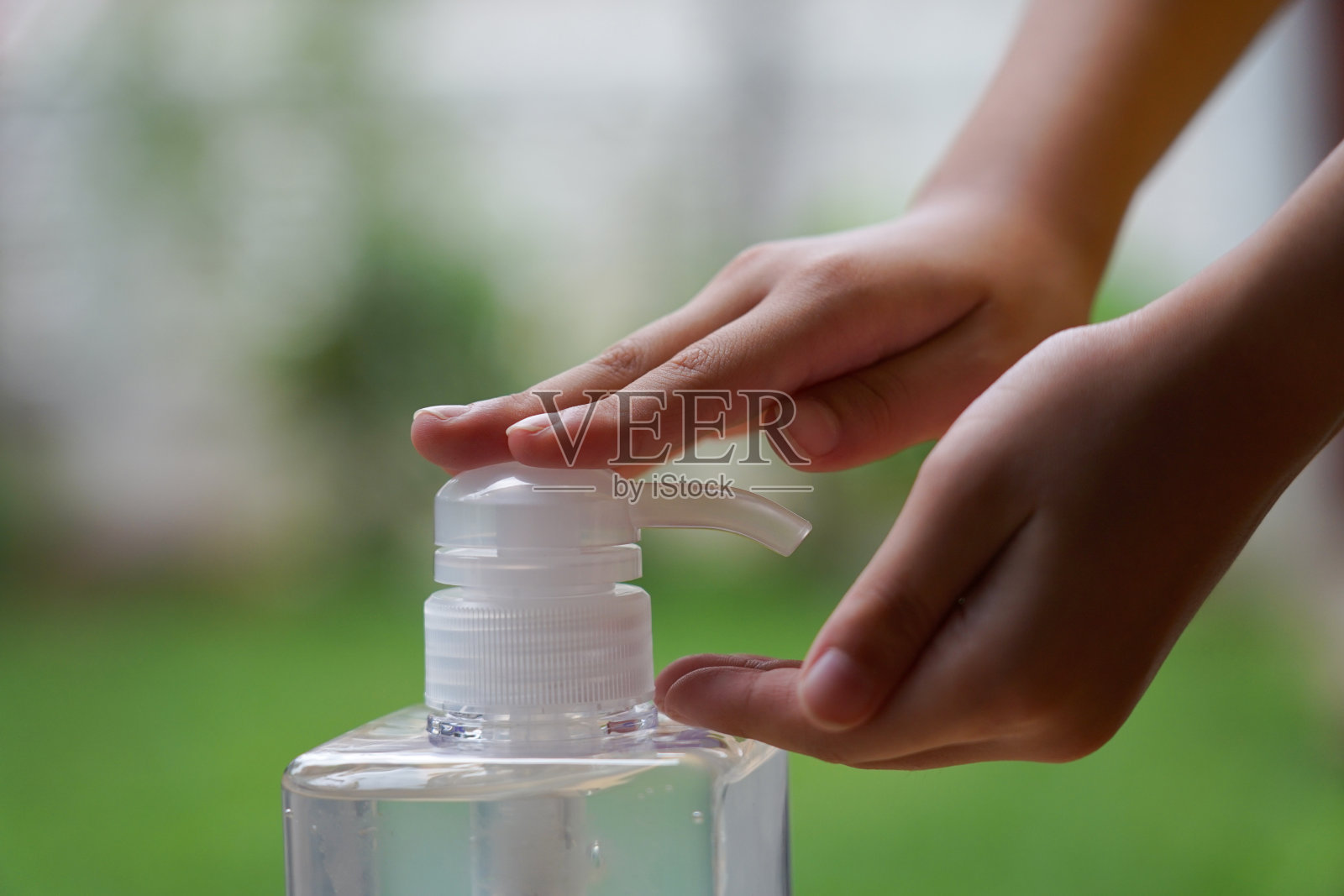 儿童双手使用酒精洗手液清洁塑料泵瓶的手，防止病毒和细菌照片摄影图片