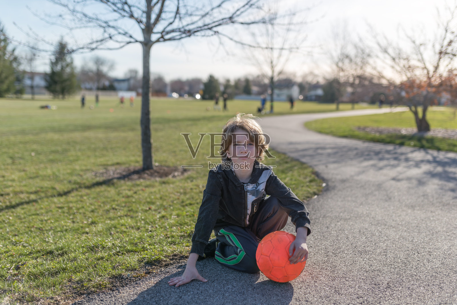 一个孩子坐在地上，手里拿着一个亮橙色的足球照片摄影图片