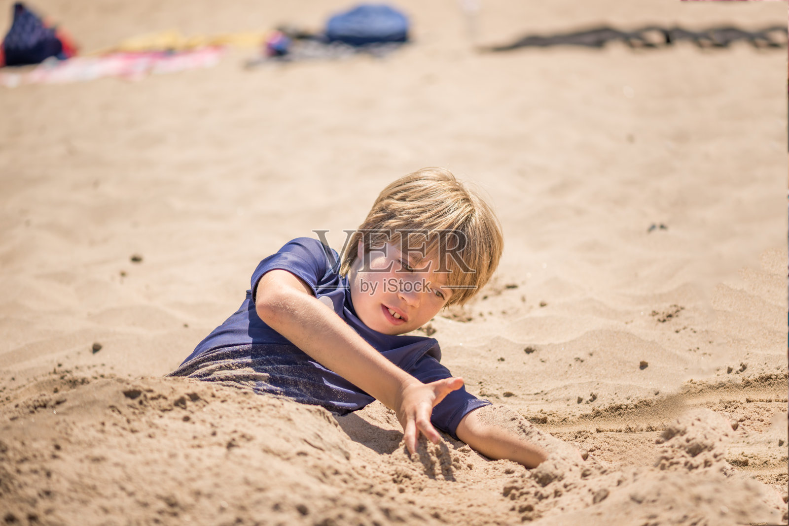 一个男孩在沙滩上玩耍，被埋在沙子里照片摄影图片
