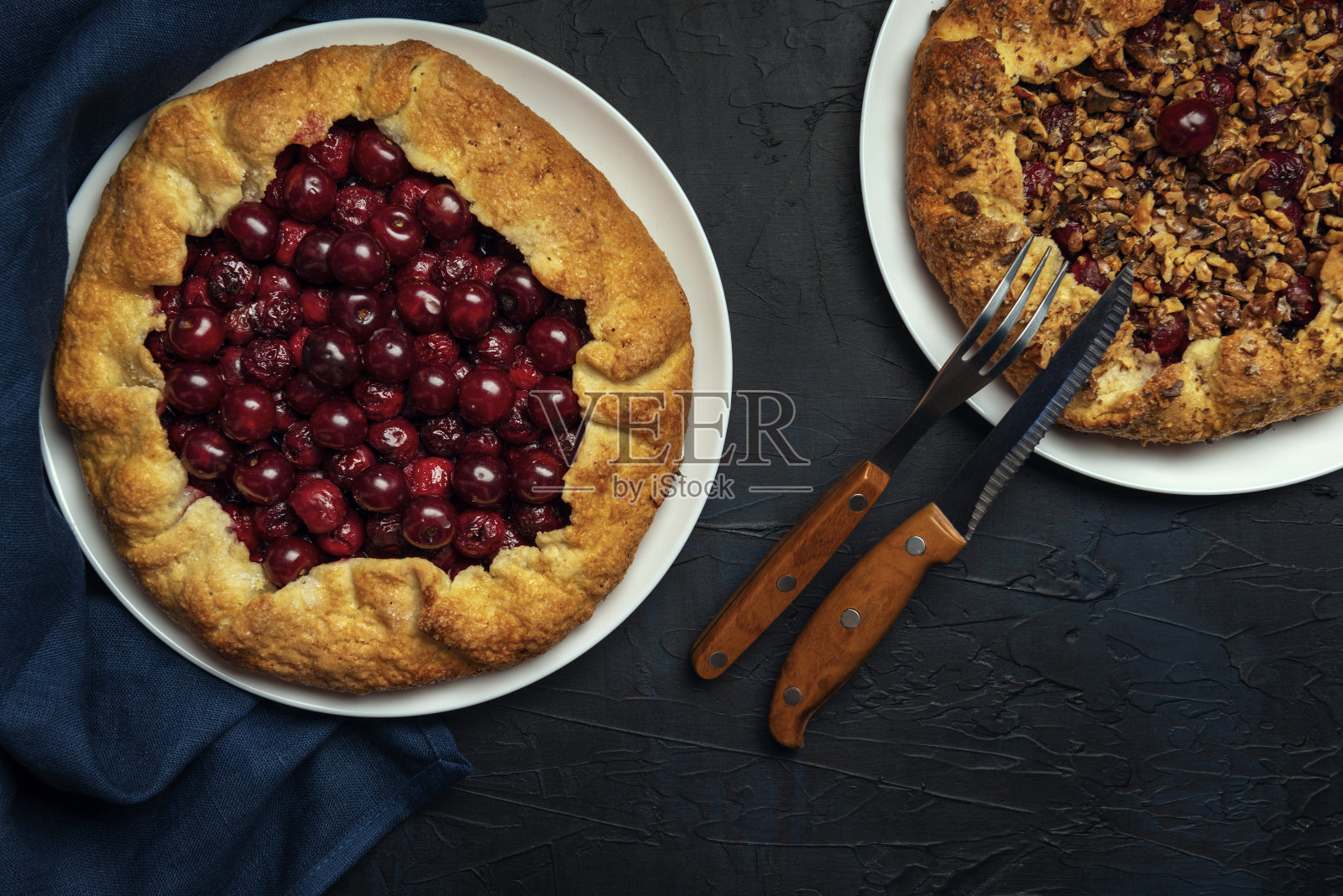 两份馅料为成熟的红樱桃和胡桃，底色为深蓝色。用餐巾和餐具自制的甜馅饼。烘焙产品。照片摄影图片
