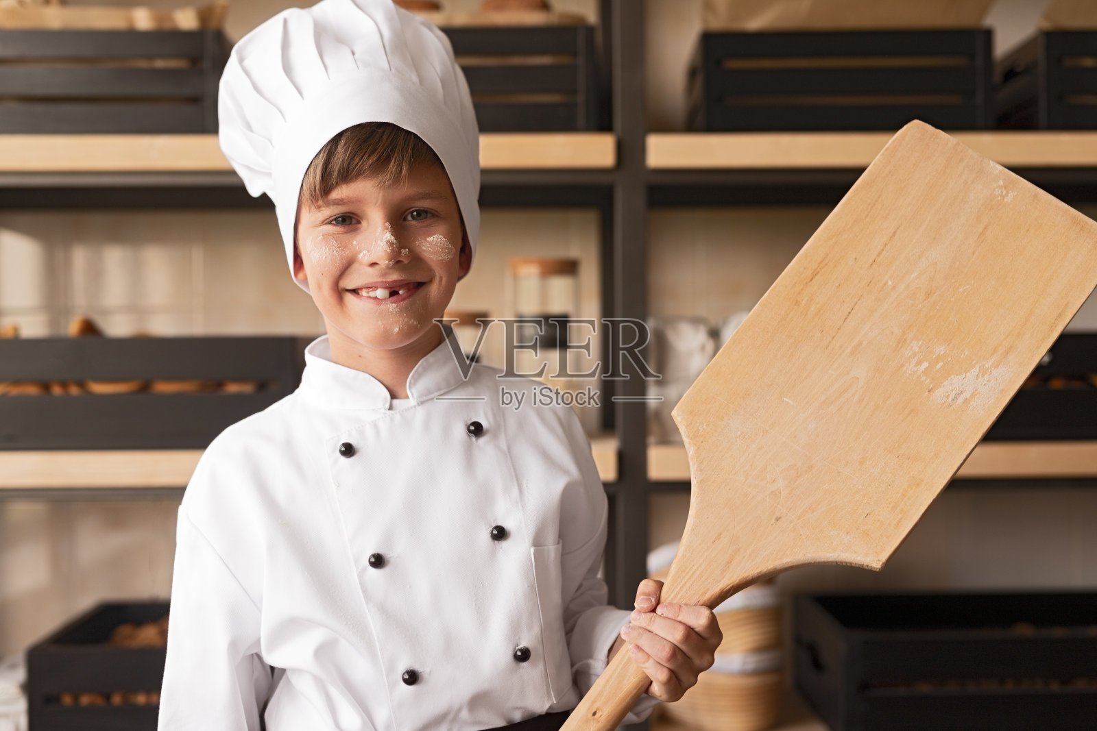 面包房里穿着厨师制服拿着铲子的快乐小孩照片摄影图片