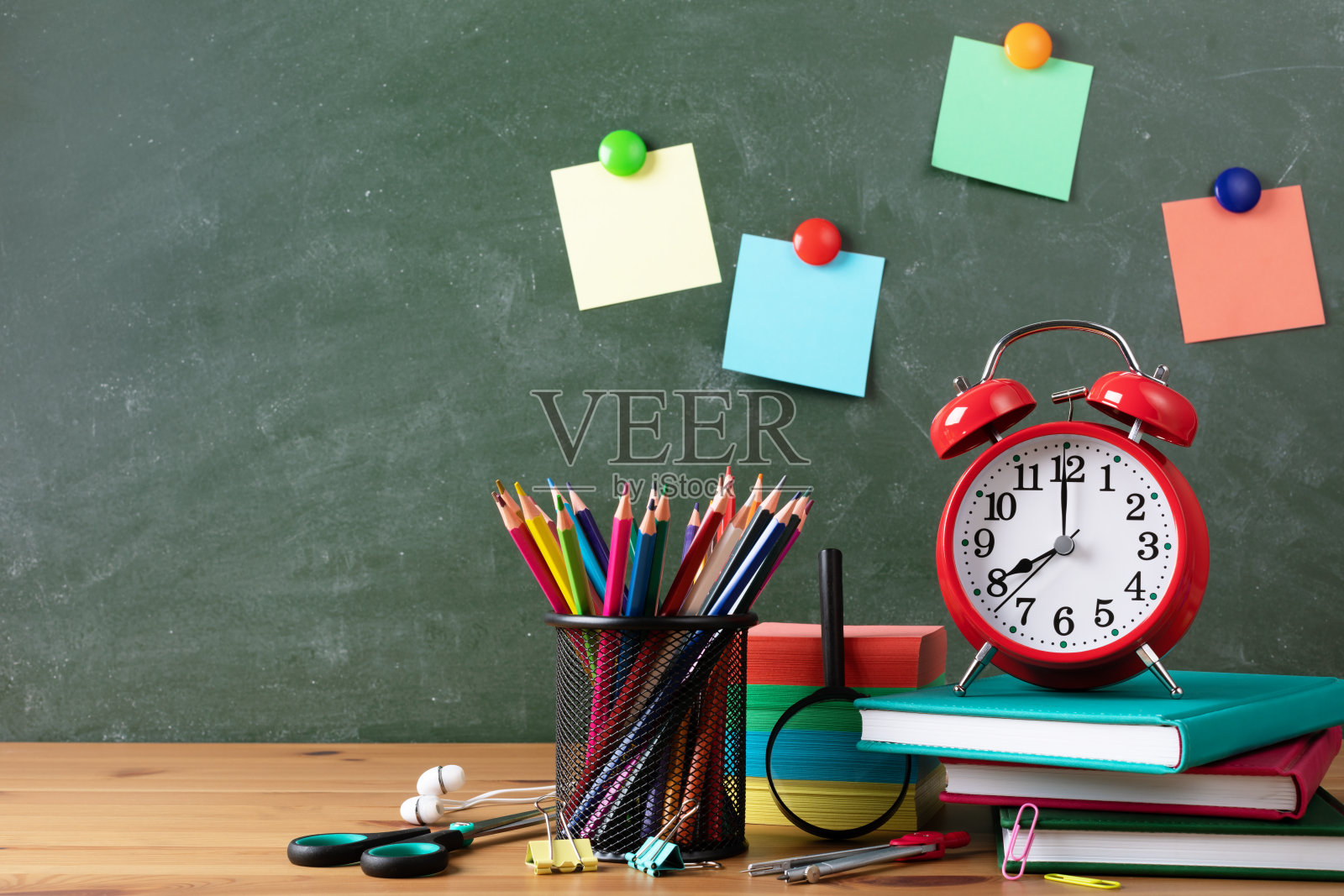 回到学校或教育理念，闹钟，纸笔记本和学校用品对黑板与彩色的笔记设计在木桌上。照片摄影图片