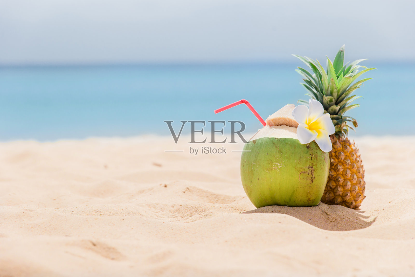 新鲜的椰子和菠萝躺在沙滩上，用吸管准备喝。热带度假旅游概念照片摄影图片