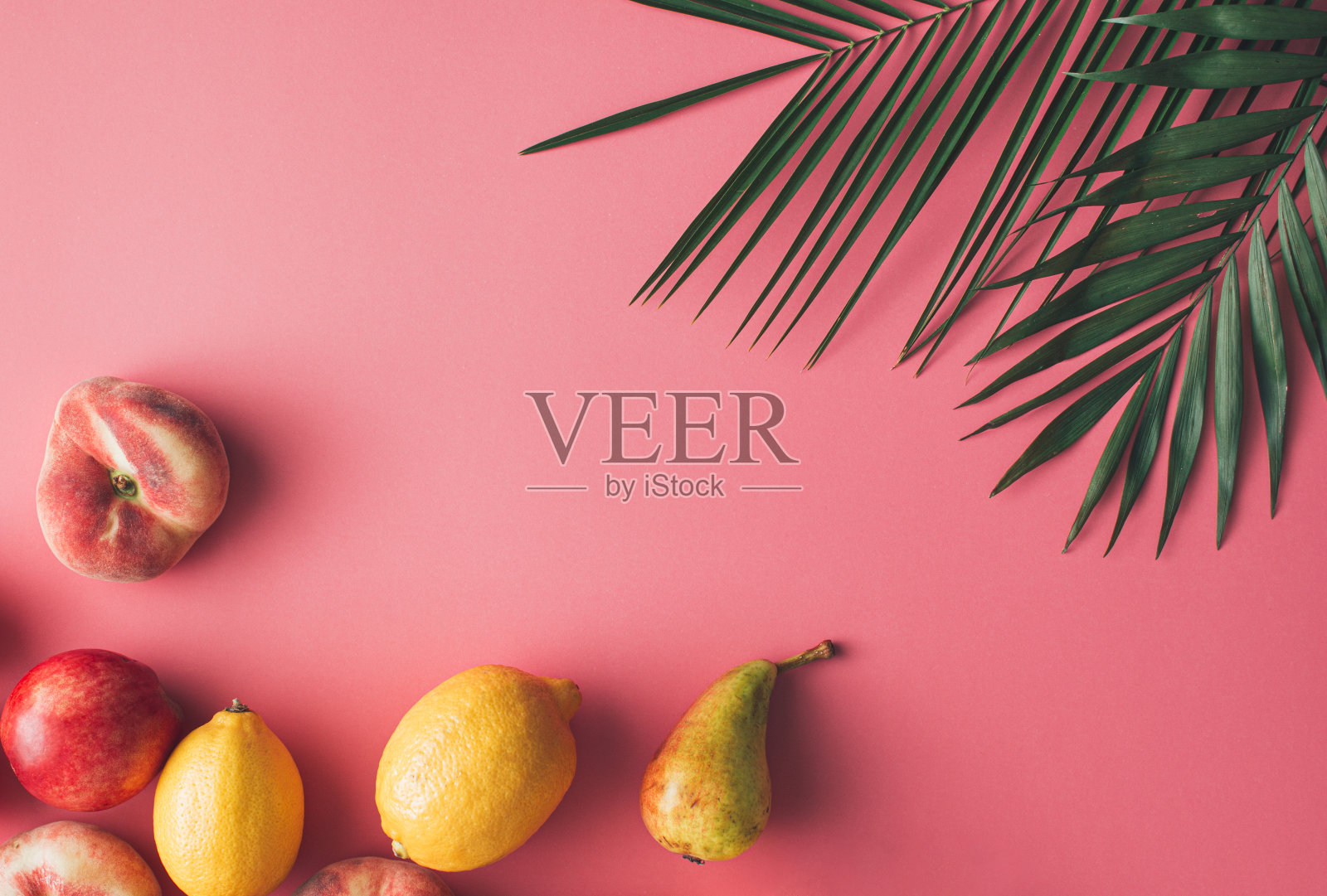 夏季热带布局，新鲜水果和绿色的棕榈叶在柔和的粉红色背景。照片摄影图片