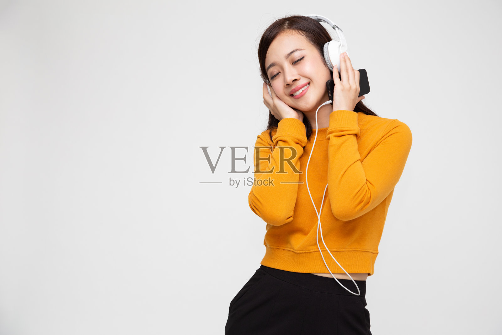 年轻的亚洲美女听音乐耳机在智能手机上播放列表歌曲应用程序孤立的白色背景照片摄影图片