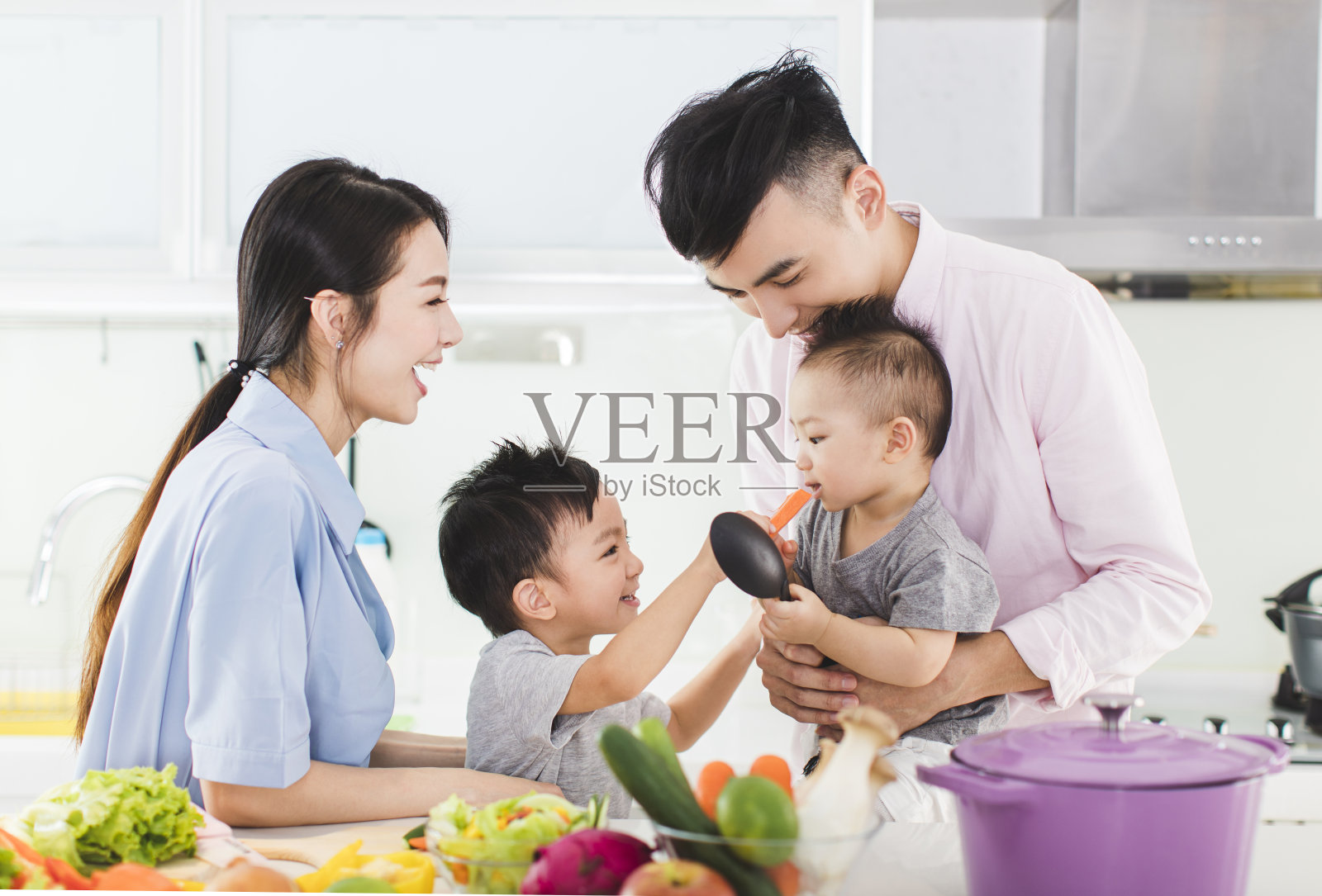 父母和儿子在厨房里喂儿子一根胡萝卜照片摄影图片