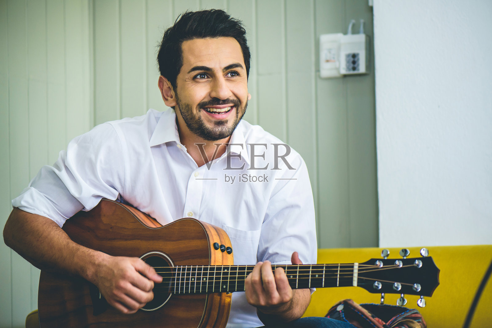 微笑迷人的男人在他的客厅的沙发上弹吉他照片摄影图片