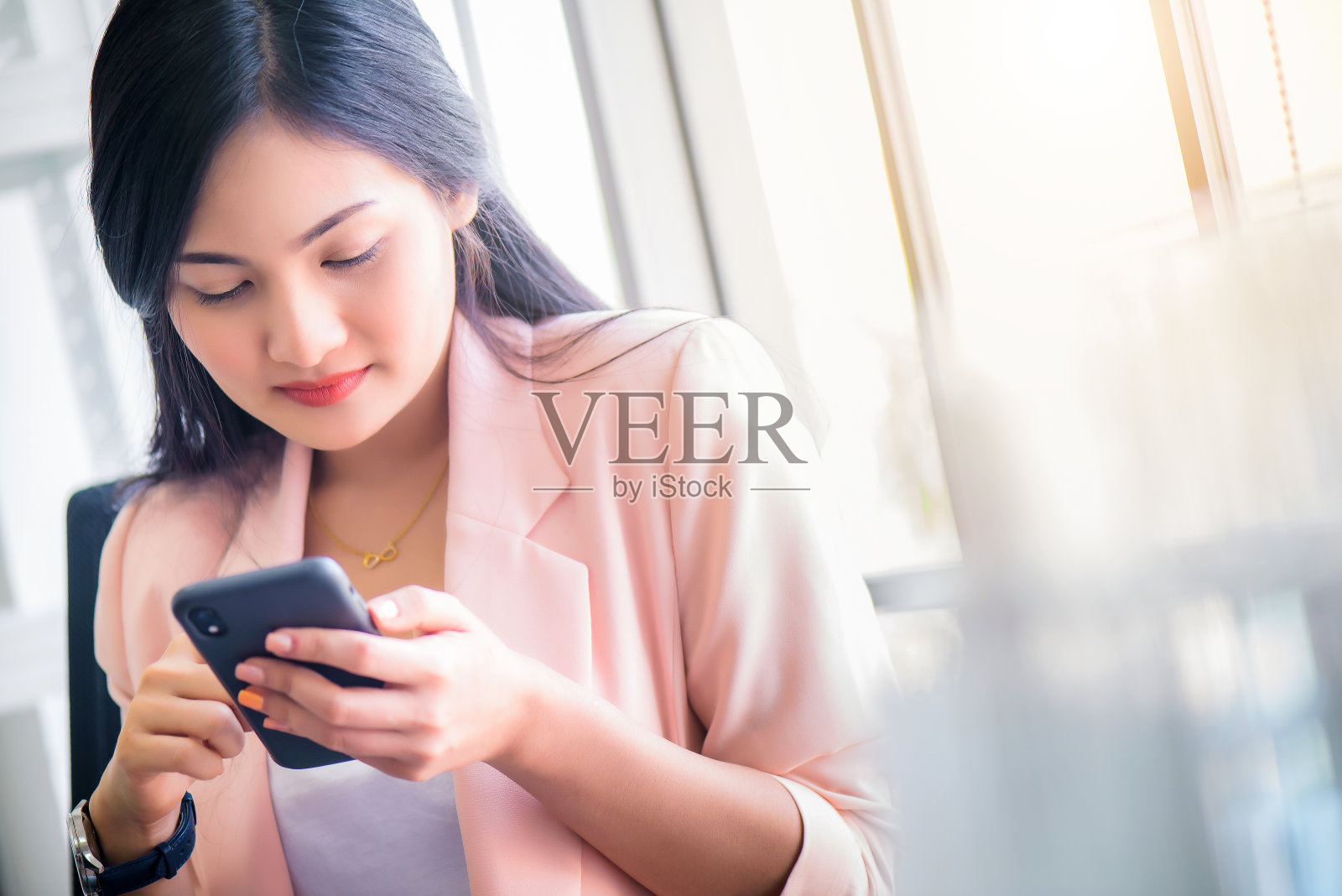 年轻美丽的亚洲女人坐在黄色沙发上，早上在客厅用智能手机或手机上网照片摄影图片