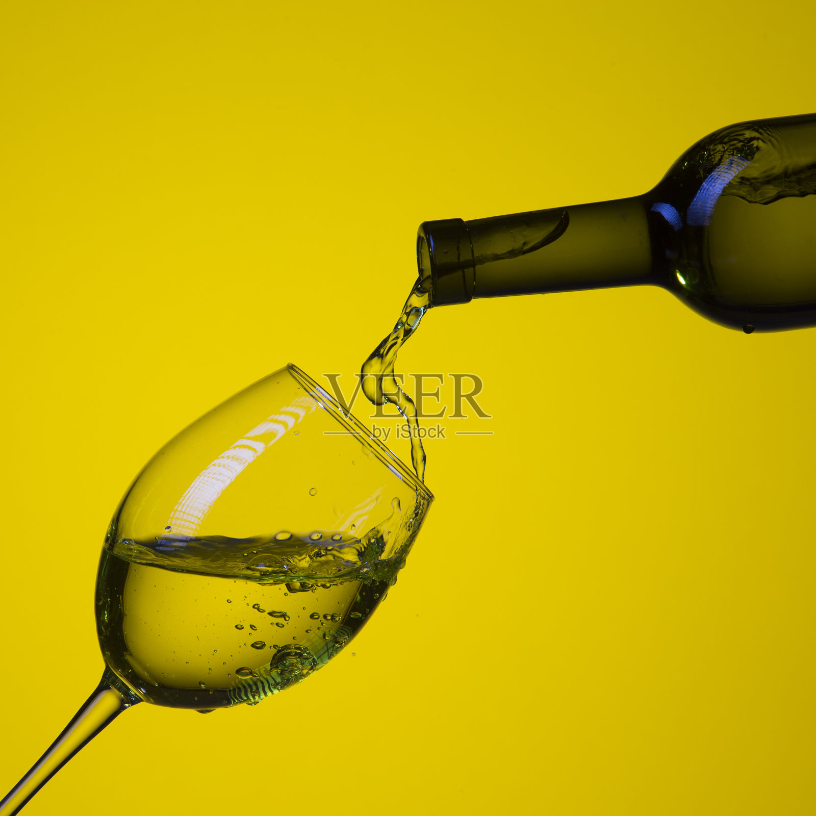 从瓶子中倒出彩色液体和水滴到酒杯中。在黄色背景上孤立。广场形象组成照片摄影图片