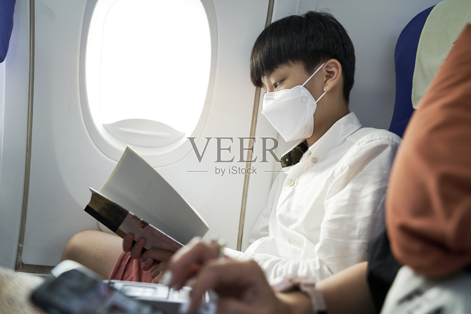 戴着面具的少年在飞机上看书照片摄影图片