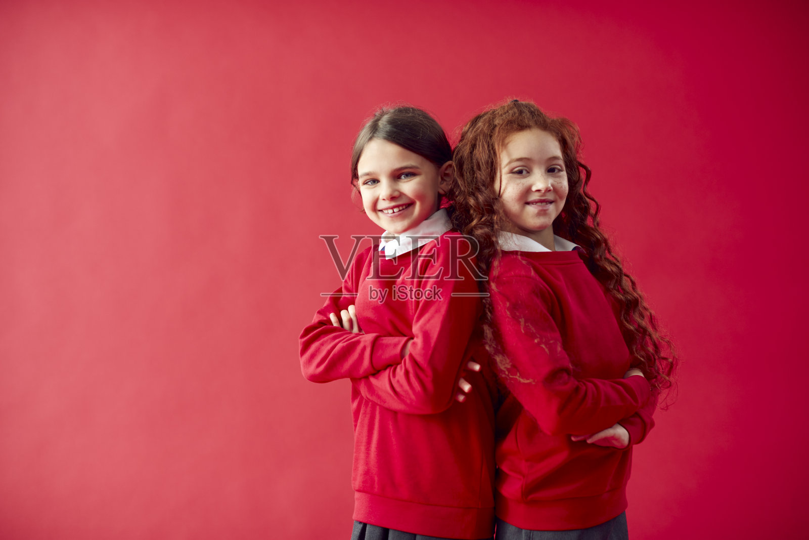 两名小学生背靠背穿著校服，背对著红色演播室背景照片摄影图片