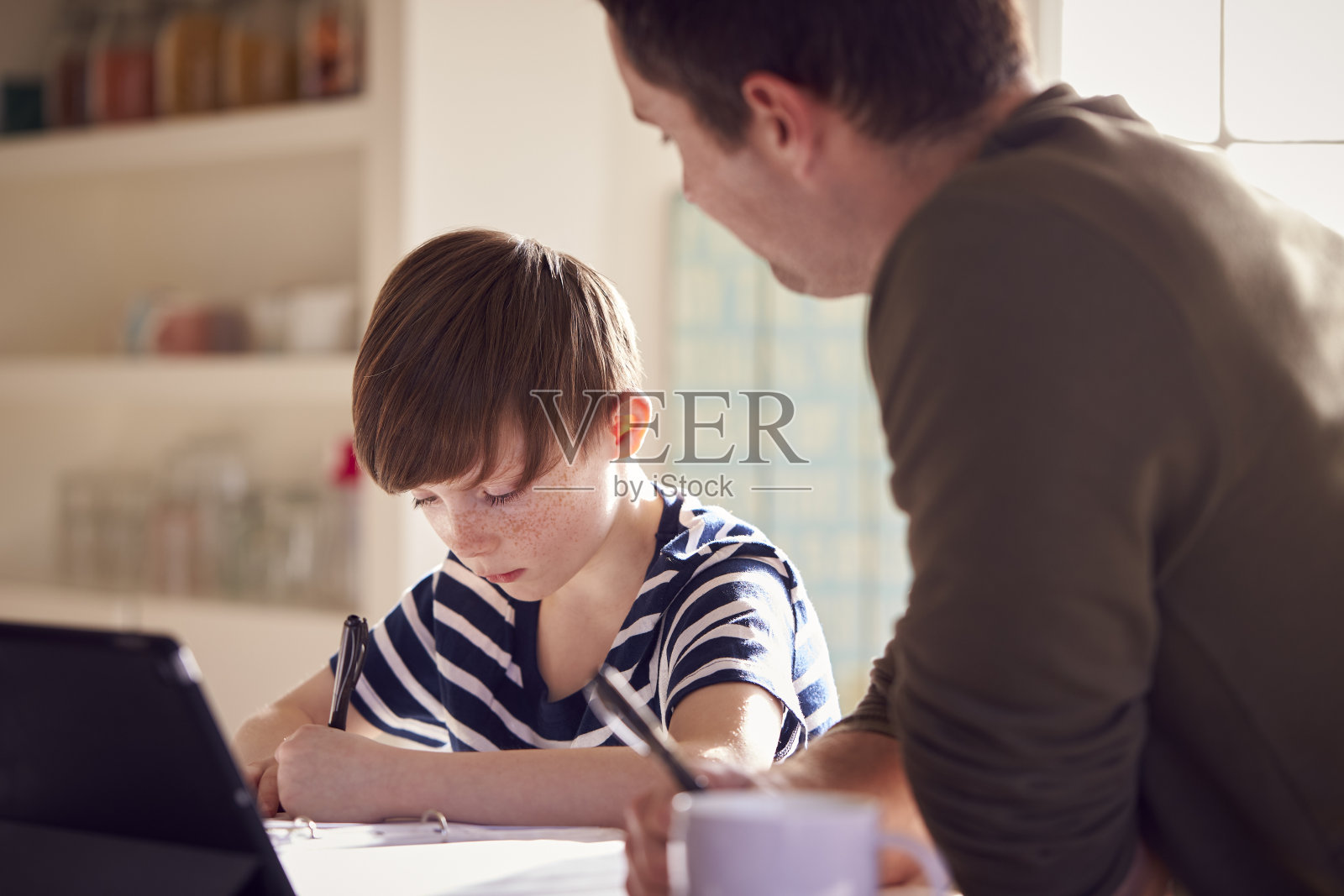 父亲帮助儿子做作业，一起坐在厨房柜台上使用数字平板电脑照片摄影图片