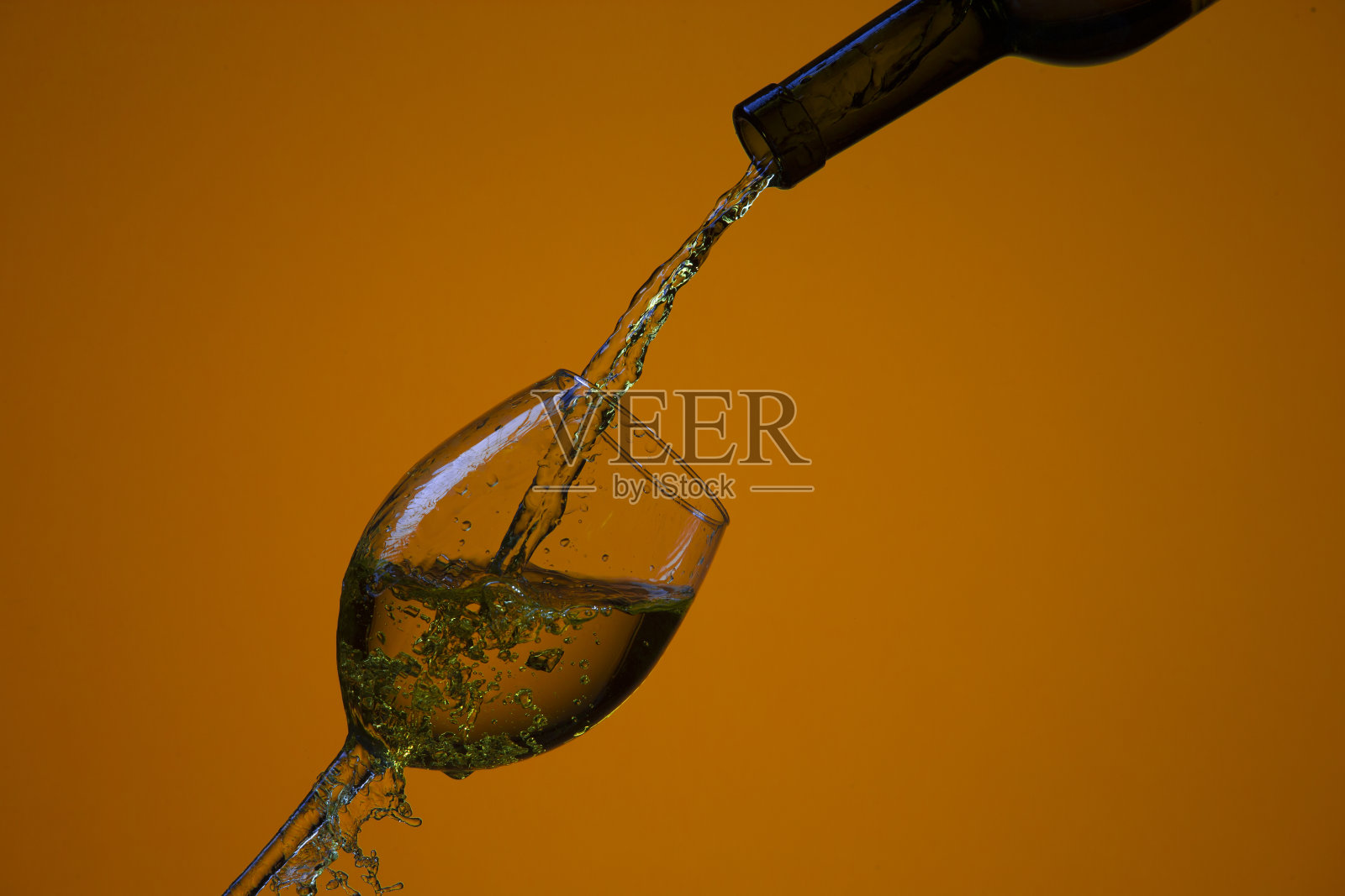 饮料倒出的瓶子在右手边的葡萄酒杯与彩色液体和水滴。水平射照片摄影图片