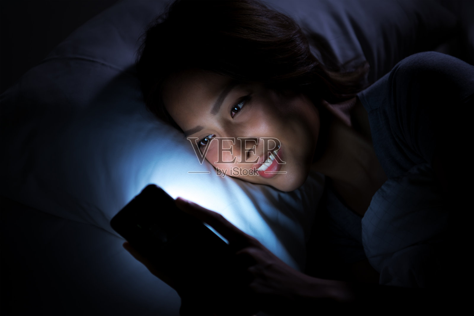 年轻女子晚上在床上用智能手机照片摄影图片