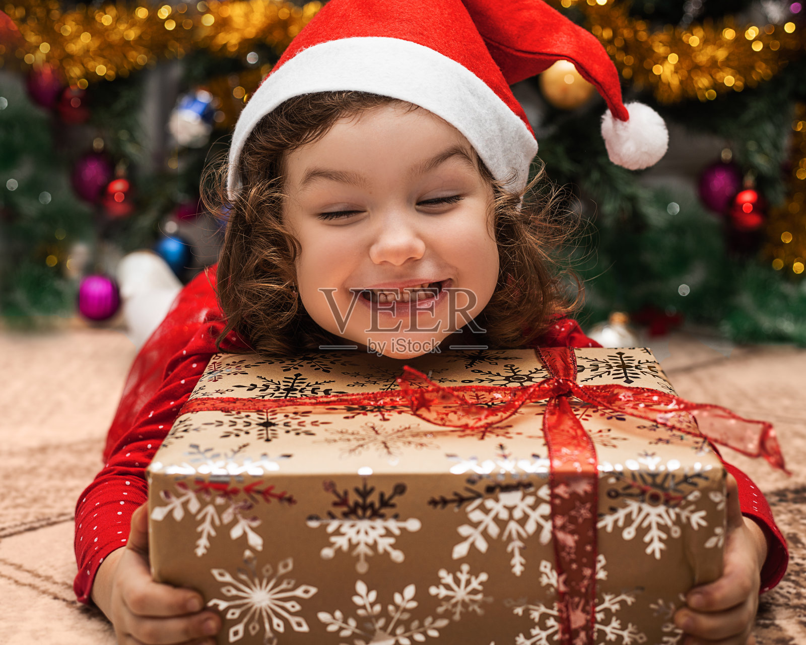 快乐的小女孩拥抱圣诞礼物在圣诞树和灯光的背景。生活特写照片在家。幽默照片摄影图片