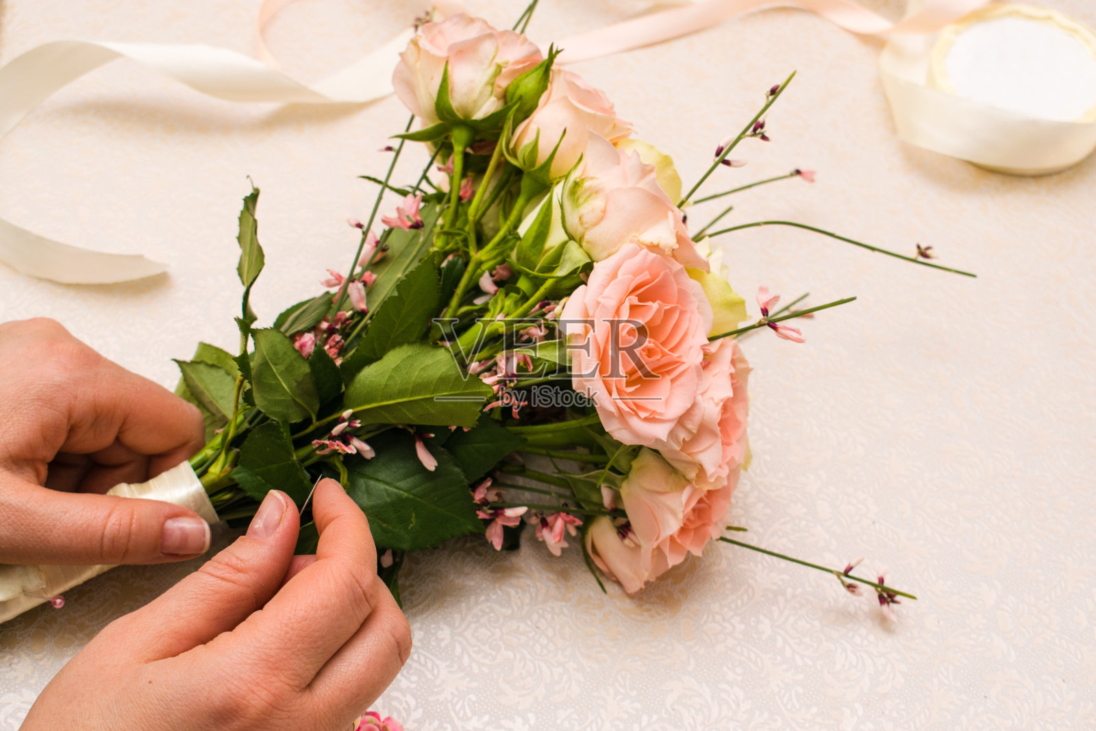 女花商的手做一个优雅的新娘花束的genista，粉色和白色的玫瑰。制作它的配件和工具都放在桌子上。俯视图照片摄影图片