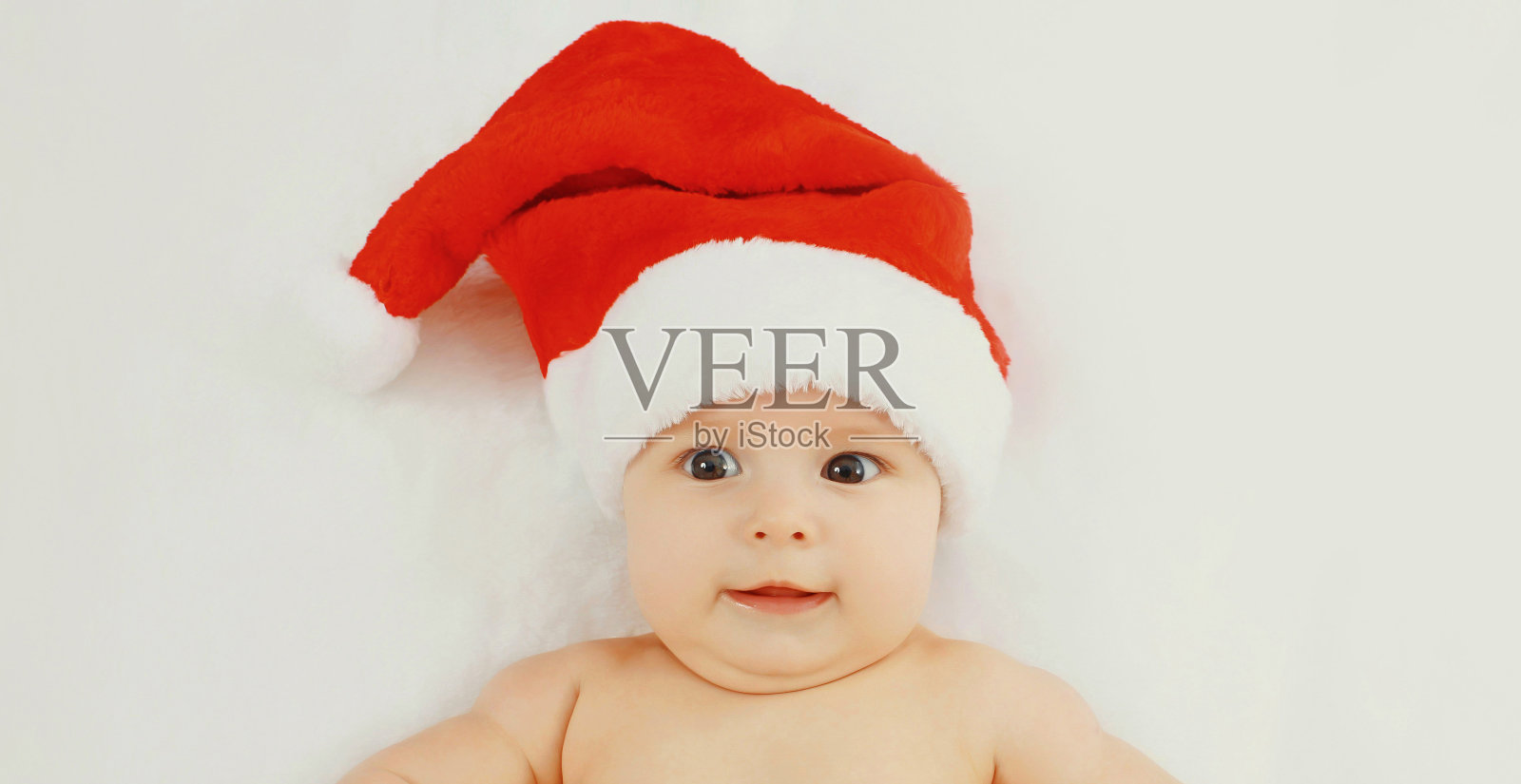 圣诞肖像快乐可爱的婴儿在红色圣诞帽躺在家里的白色床上照片摄影图片