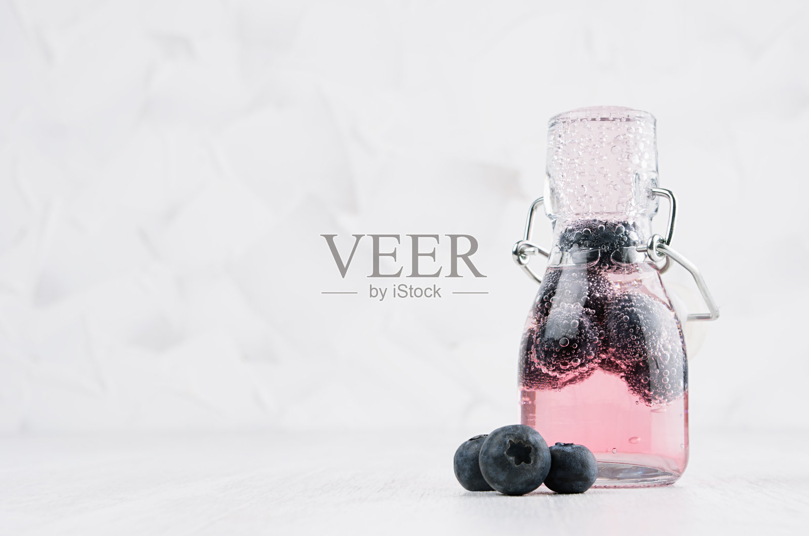 清爽的冷水果粉色饮料与蓝莓，明亮的气泡在透明的轭瓶在优雅的白色内饰木桌子，复制空间。照片摄影图片