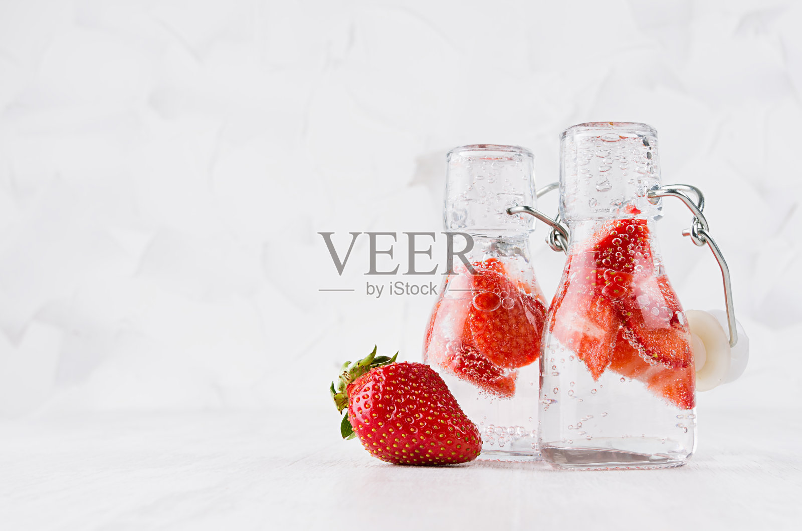 天然有机鸡尾酒草莓，碳酸水在两个轭瓶明亮的白色木板和墙壁，复制空间。照片摄影图片