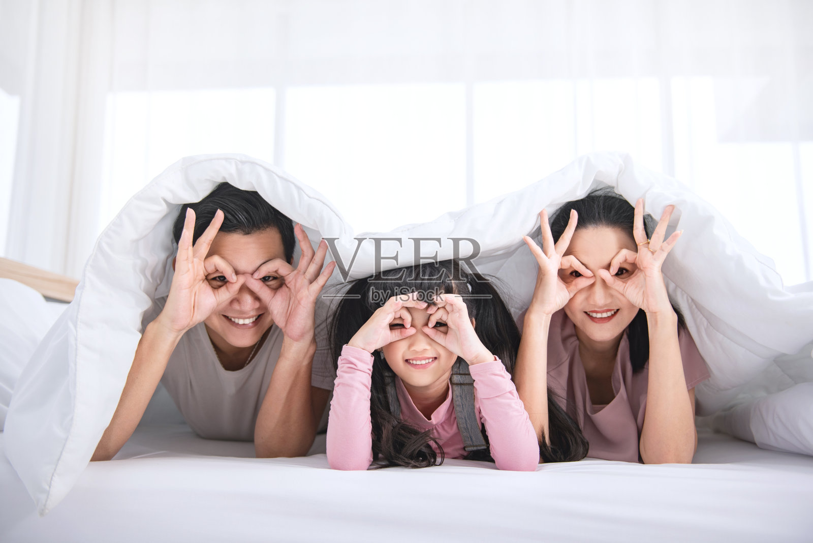 幸福的亚洲家庭躺在床上，在家里的卧室里微笑。照片摄影图片
