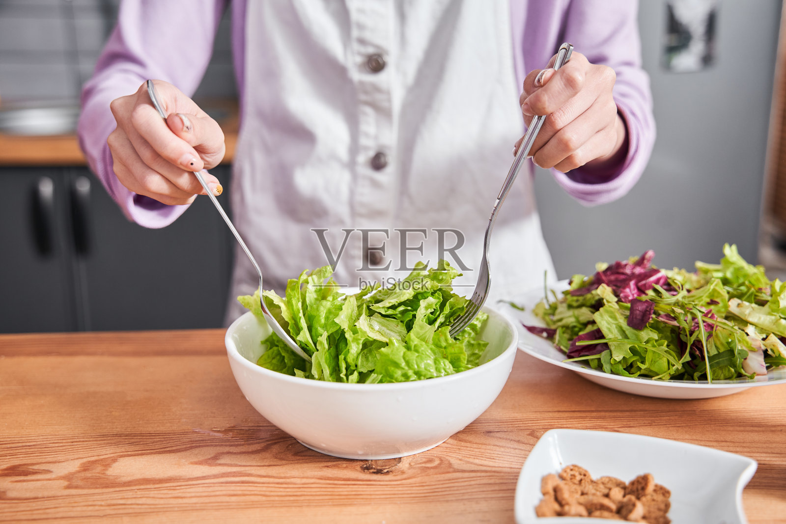 女人在准备沙拉的时候，把沙拉放在桌上的碗里照片摄影图片