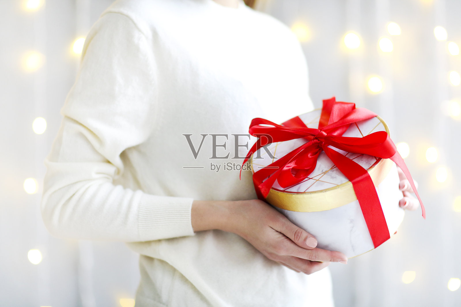 在节日庆祝中，穿着白色毛衣的女孩拿着用鲜红丝带系着的礼物盒照片摄影图片