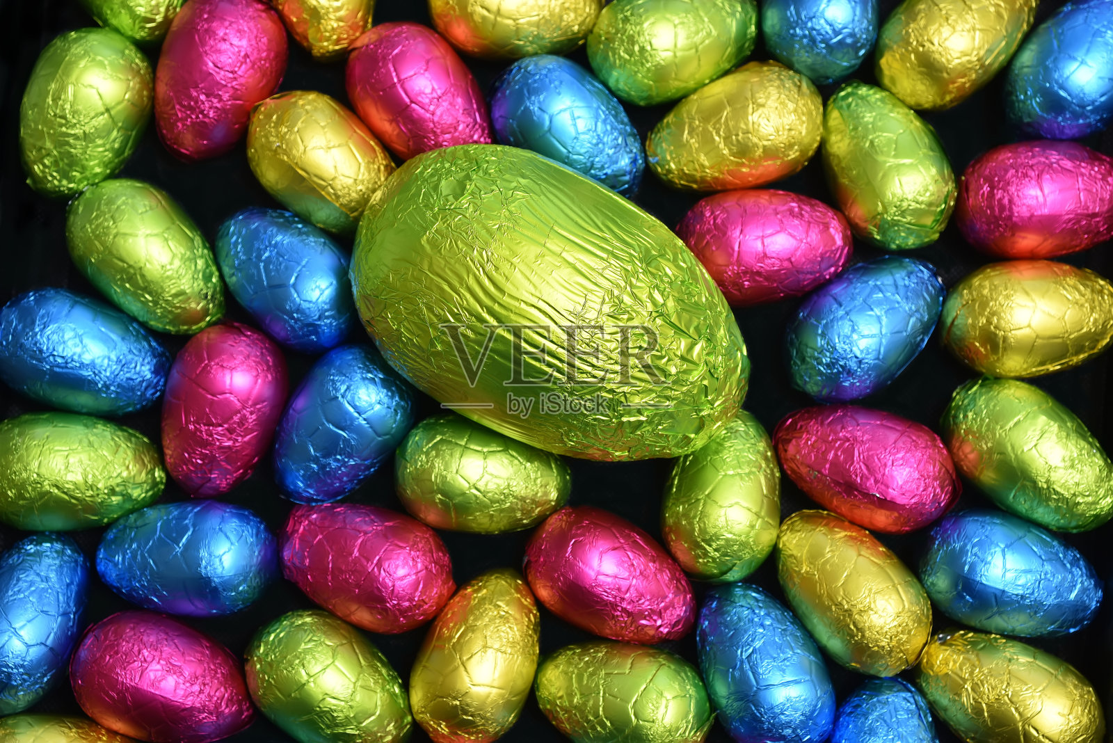 1 .用锡箔纸包裹一堆或一组各种颜色、不同大小的巧克力复活节彩蛋，彩蛋的颜色有粉色、蓝色、黄色和酸橙绿，中间放一个绿色的大鸡蛋。照片摄影图片