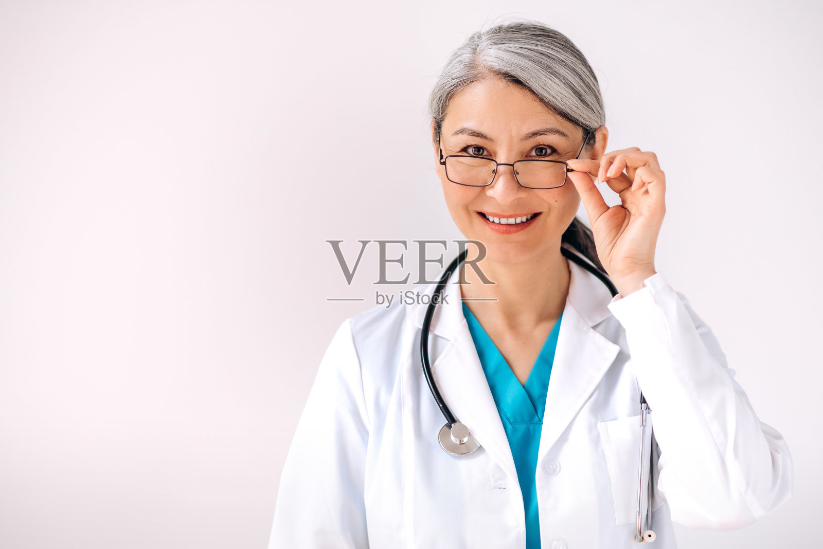 身着医疗服，手持听诊器，站在白色背景下，看着镜头微笑的白人女医生的特写照片。医疗保健的概念照片摄影图片