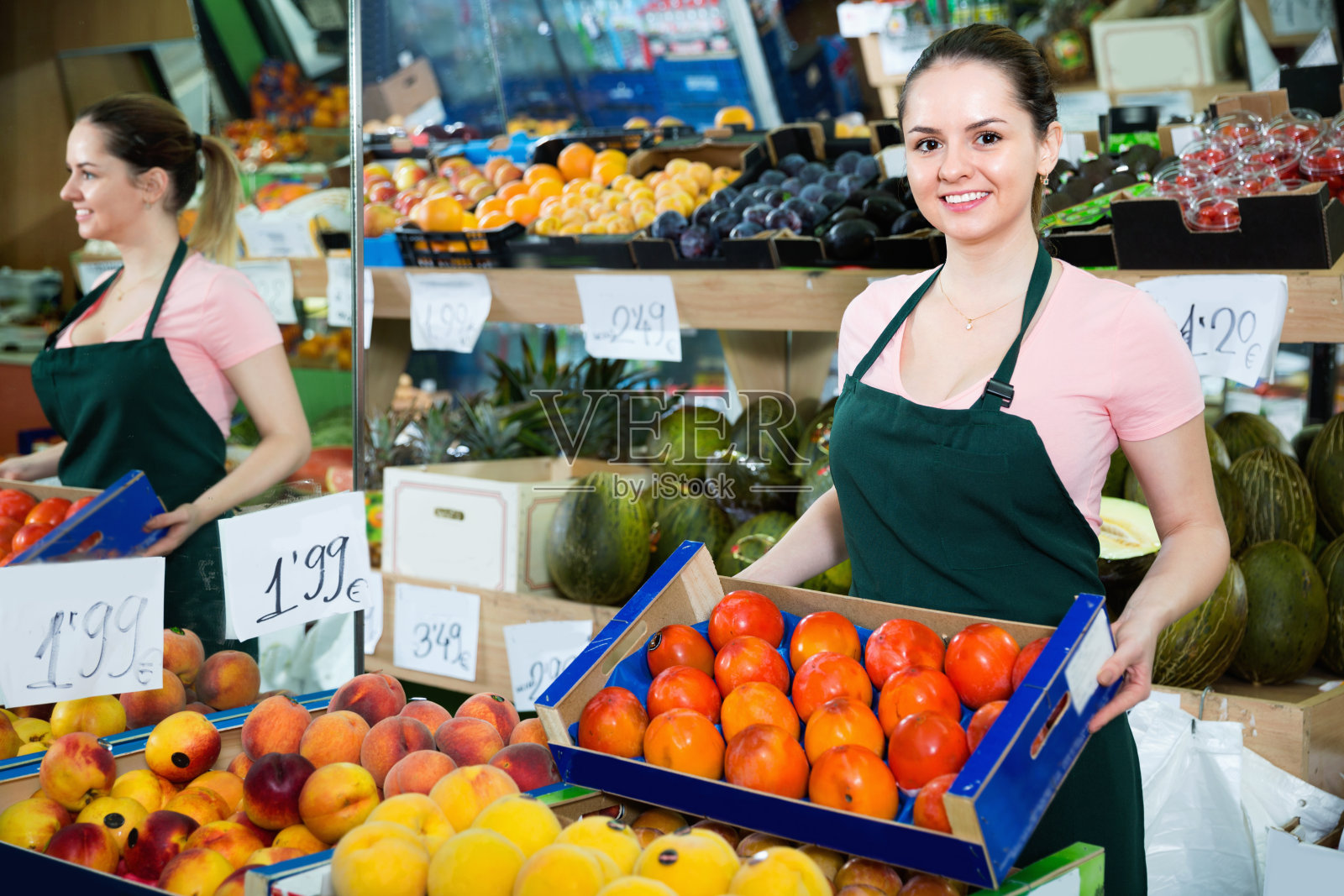 年轻的女售货员面带微笑，手里拿着一盒成熟的橘子柿子照片摄影图片